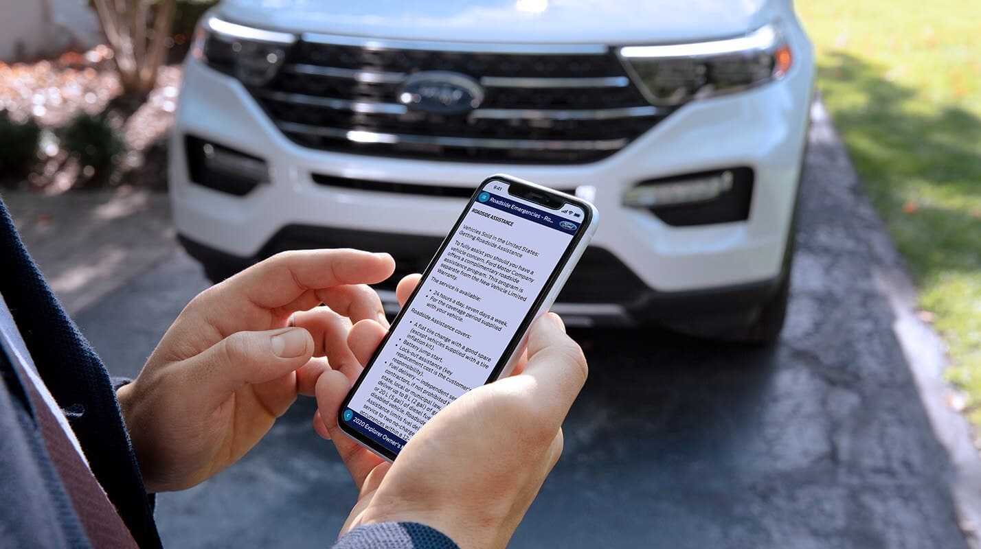 A person stands in front of a white Ford SUV in Mississauga, holding and looking at a smartphone displaying a detailed customer service message on the screen.