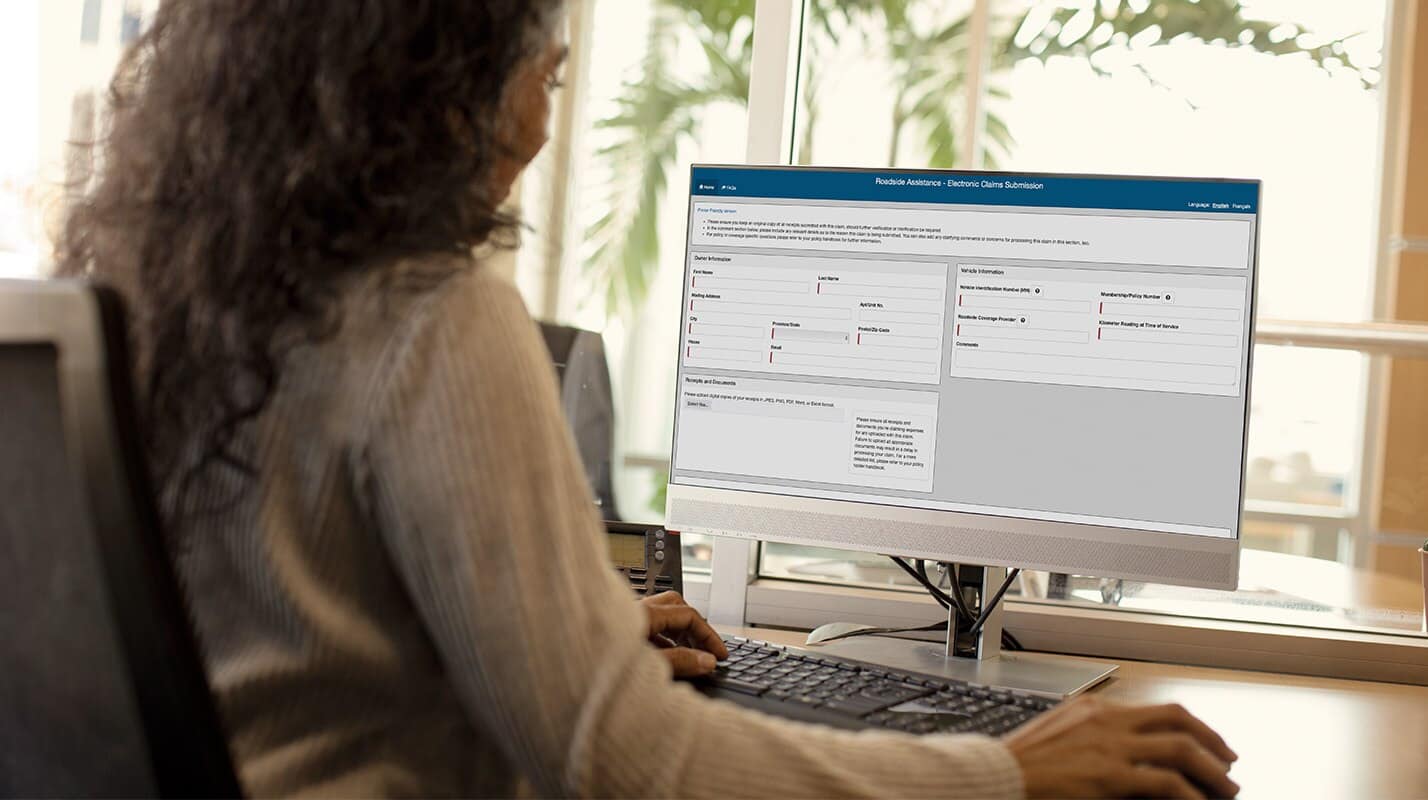 A person with long curly hair sits at a desk in Mississauga, working on a desktop computer and viewing a Leadbox Dealer online submission form. A window and some green plants are visible in the background.