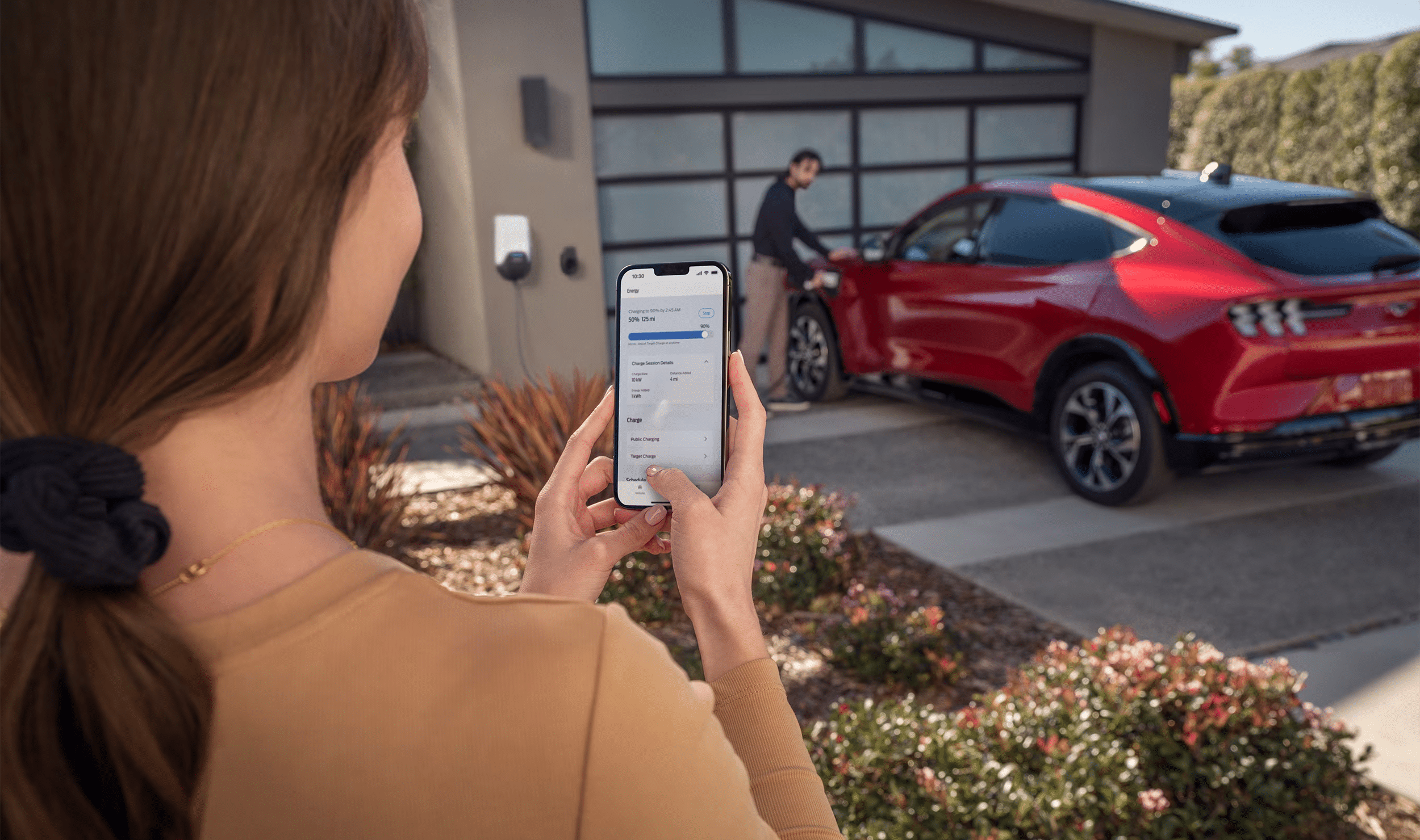 Woman using FordPass app on her phone to check charge level of red Mustang Mach-E in background.