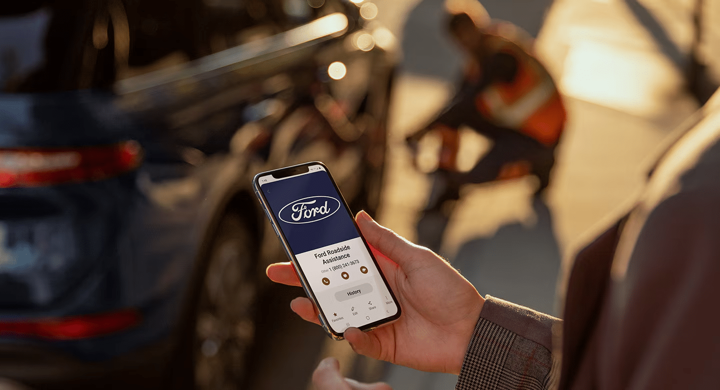 A woman leans against a vehicle while using a smartphone.