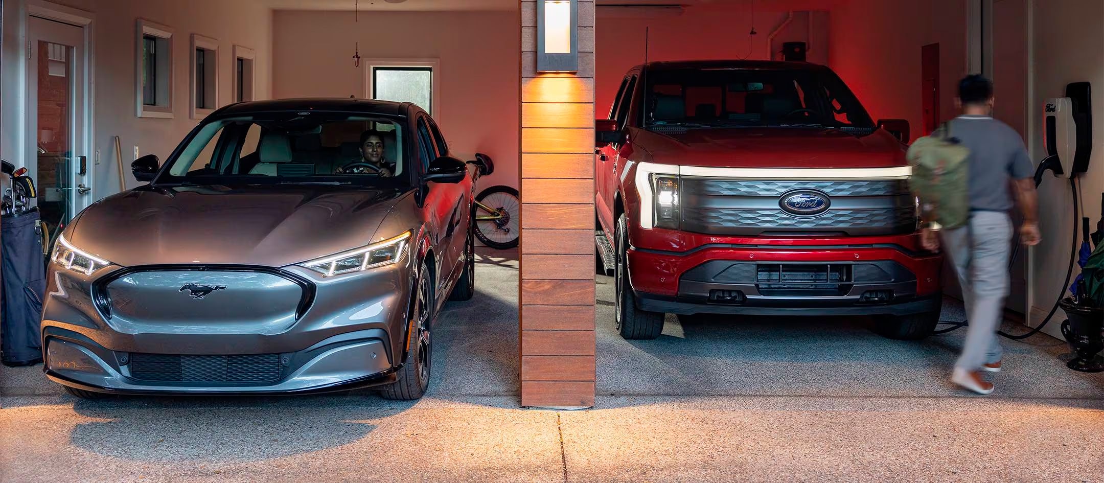 A Ford Mustang Mach-E SUV and Ford F-150 Lightning are parked in an open garage. 
