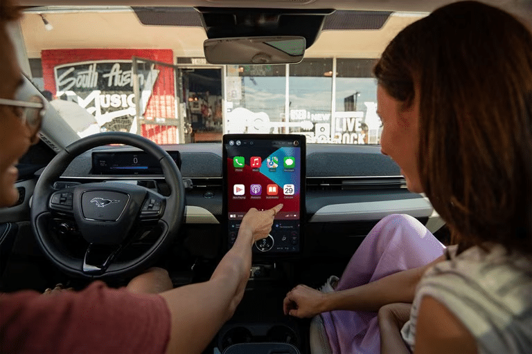 A driver and passenger happily play a game together on the in-vehicle touchscreen of a Ford Mustang Mach-E. 