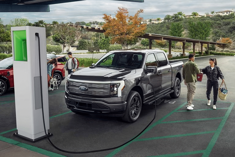 A man checks his phone in front of an EV charger that is charging a Ford F-150® Lightning® truck. 