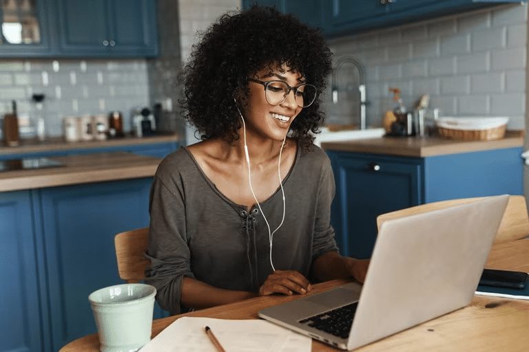 A woman checks her phone in front of a laptop stand at her desk. 