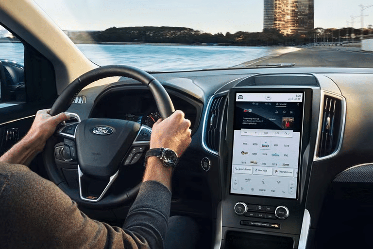 Person driving a Ford vehicle with the screen displaying the SiriusXM interface.