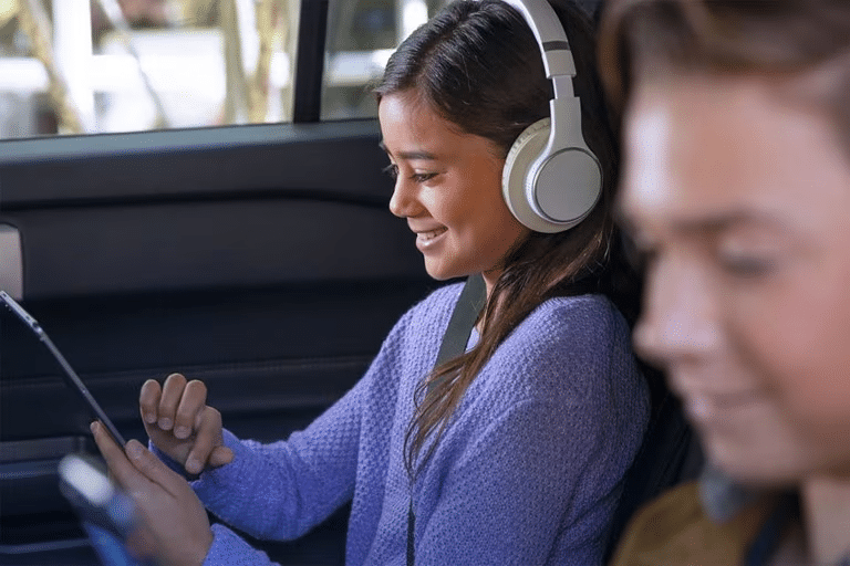 Two smiling children using mobile devices while sitting in the second and third rows of a Ford SUV.