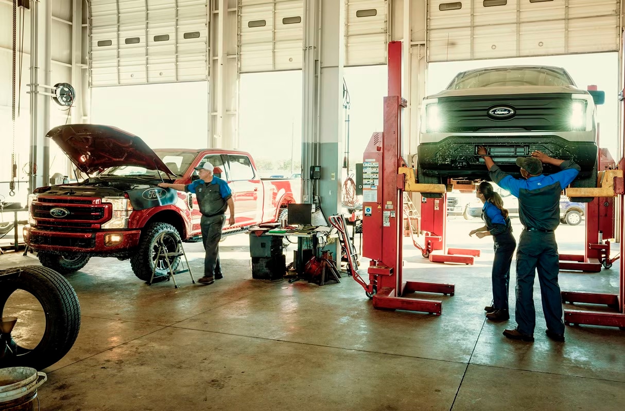 Ford Pro™ technicians working on vehicles inside a large service garage.