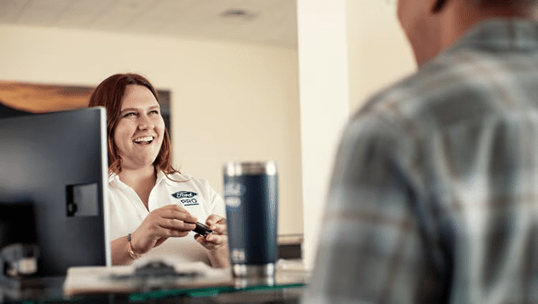 Smiling female Ford Pro™ employee standing behind a desk and talking to a male customer.