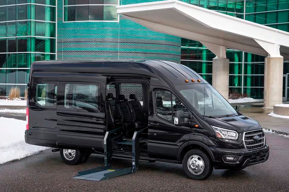 A black Ford Transit with its side door open showing a wheelchair platform lift.