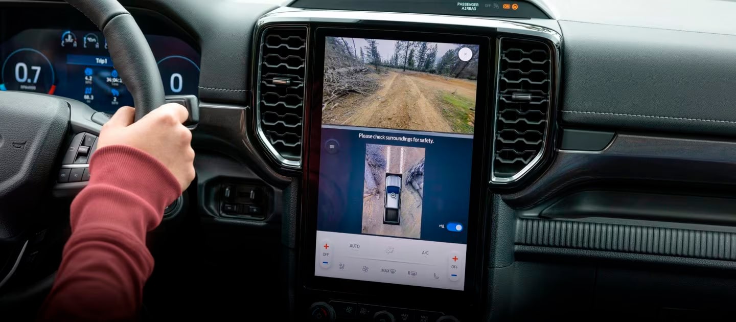  A driver using the backup camera on a Ford vehicle's infotainment screen to assist with parking.