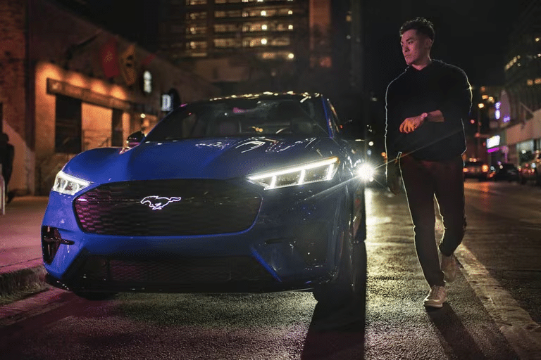A person walks beside a Ford Mustang parked on an urban street at night.